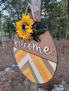 a wooden welcome sign with sunflowers and leaves hanging from it's side