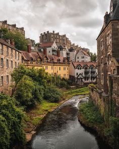 a river running through a lush green hillside next to tall brick buildings and small trees