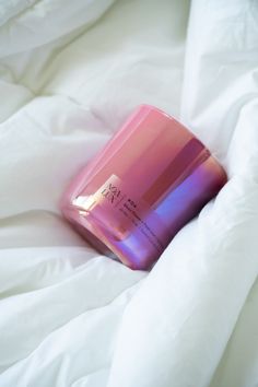 a pink and purple container sitting on top of a white bed sheet covered in sheets