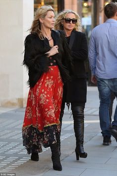 two women are walking down the street with one woman in black jacket and red dress