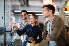 three people standing in front of a glass wall and looking at something on the screen