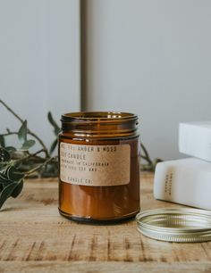 a candle sitting on top of a wooden table next to a white box and plant