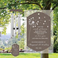 a memorial wind chime hanging from a tree in front of a field with trees