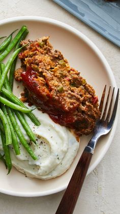 a white plate topped with green beans and meatloaf next to mashed potatoes