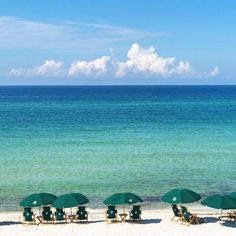 several lawn chairs and umbrellas are on the beach near the blue ocean with clouds in the sky