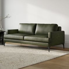 a green leather couch sitting on top of a wooden floor next to a white rug