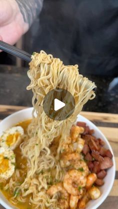 someone is holding chopsticks over a bowl of noodles with shrimp, eggs and beans