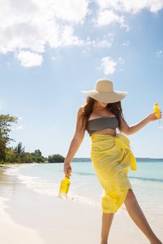 a woman walking on the beach with a drink in her hand and a straw hat