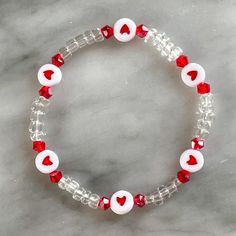 a red and white beaded bracelet with heart charms on it's end, sitting on a marble surface