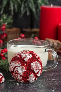 a red and white cookie next to a glass of milk on a table with christmas decorations