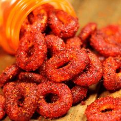 a pile of red food sitting on top of a wooden table next to a bottle