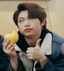 a young man is holding an apple and giving the peace sign with his hand while sitting down