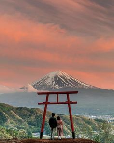 two people standing in front of a red chair with a mountain in the back ground