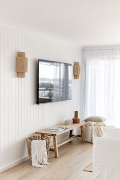 a living room with white walls and wooden furniture, including a flat screen tv mounted on the wall