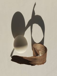 an egg is casting a shadow on the wall next to a piece of wood that has been cut in half