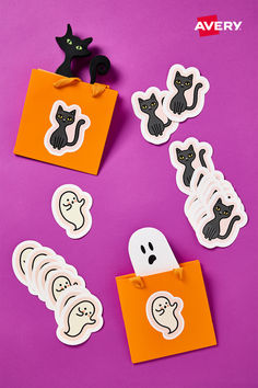 halloween stickers with black cats and ghostes on purple paper, next to an orange bag