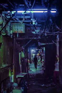 people are walking down an alley way in the dark with neon lights on them and garbage everywhere