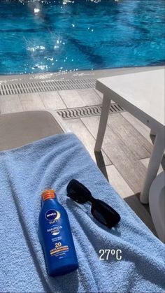 a bottle of sunscreen and sunglasses sitting on a towel next to a swimming pool