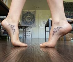 two people with tattoos on their feet standing on a wooden floor