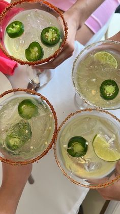 three people are holding glasses with drinks and limes on the table in front of them