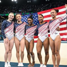 four women standing in front of an american flag and holding up their arms with both hands