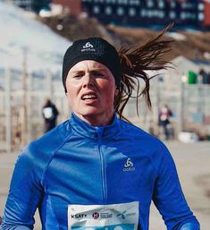 a woman running with her hair blowing in the wind while wearing a blue shirt and black beanie