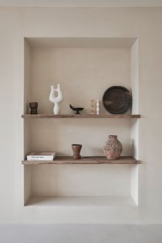 two shelves with vases and other items on them in a room that has white walls