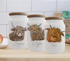 three glass jars with cows painted on them sitting on a counter next to an apple