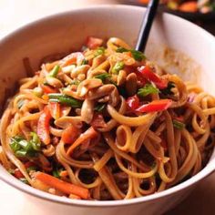 a white bowl filled with noodles and vegetables on top of a wooden table next to a skillet