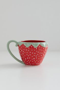 a red and white polka dot coffee cup with green trim on the rim, sitting on a table