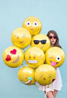 a woman in sunglasses is holding some yellow balloons with emoticting faces on them