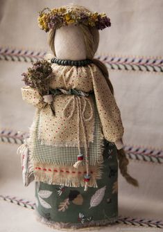 a doll is dressed in an old fashioned dress and has flowers on her head, sitting on a table