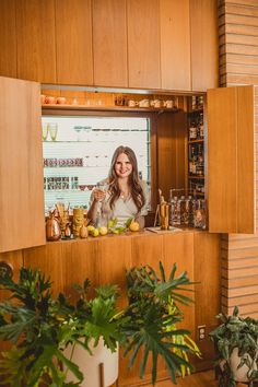 a woman standing in front of a counter filled with fruit and drinks on top of wooden cabinets