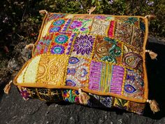 a multicolored patchwork pillow sitting on top of a rock