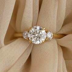 an engagement ring with three stones on top of it, sitting on a beige cloth