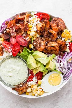 a salad with shrimp, avocado, corn, tomatoes and dressing in a white bowl