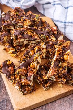 homemade granola bars with chocolate drizzled over them on a wooden cutting board