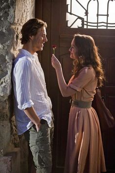 a man standing next to a woman holding a flower in her hand and looking at him