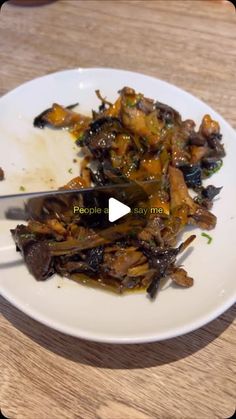 a white plate topped with cooked vegetables on top of a wooden table next to a knife