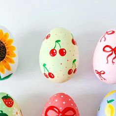 painted eggs with bows and cherries are arranged in a row on a white surface