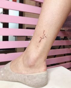 a woman's foot with a small tattoo on her left ankle, sitting in front of a pink chair