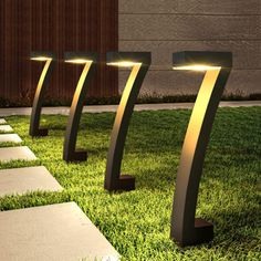 three modern outdoor lights in the grass near some steps and walkways at night time