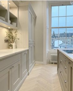 a large kitchen with white cabinets and wood flooring next to a window overlooking the city