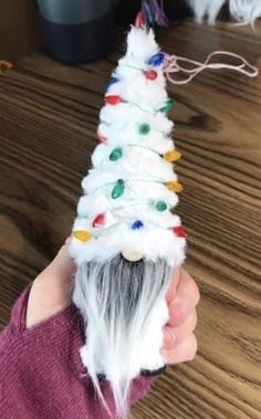 a hand holding a white christmas tree made out of yarn on top of a wooden table