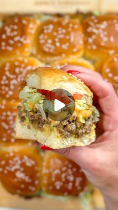 a hand holding a hamburger with cheese and olives