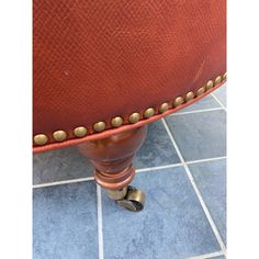 an upholstered red leather chair with brass studded trim and foot rests on a blue tile floor