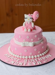 a hello kitty birthday cake with pink frosting and white flowers on the bottom tier