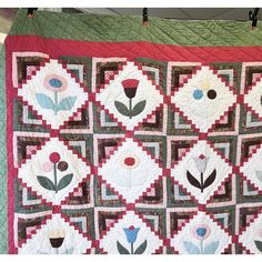 a quilted wall hanging on the side of a building with flowers and leaves painted on it