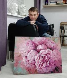 a man sitting in a chair next to a large pink flower on a canvas that has been painted with acrylic paint