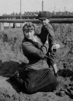 an old black and white photo of a woman holding a child on her lap, with pipes in the background